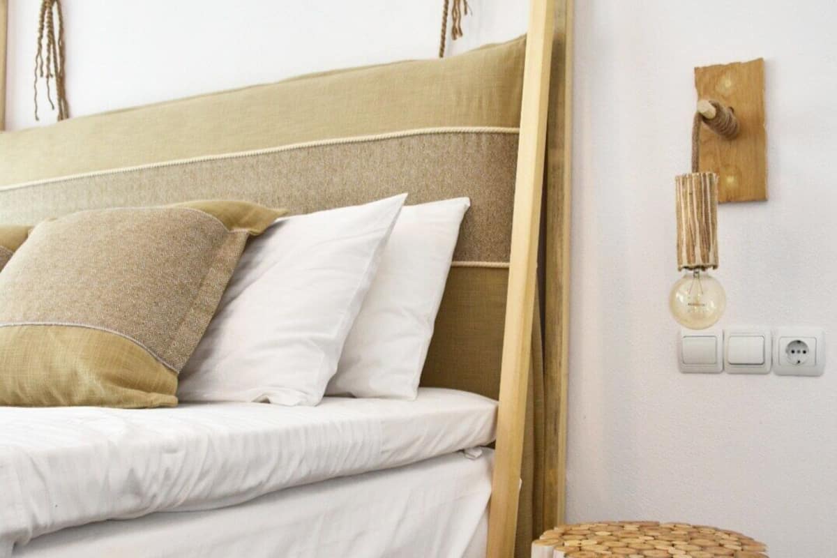 A bed with a wooden headboard, white bedding, and a round wooden stool.