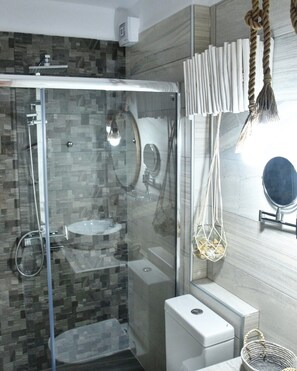 A modern bathroom with a glass-enclosed shower, a white toilet, and a vanity with a mirror. - Angelos Boutique Suites (Alonissos)