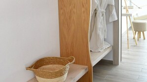 Een houten bank met een gevlochten mand, een badjas aan een rek, en een kijkje in een kamer met een schilderij en een stoel.