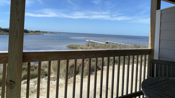 A wooden deck with a view of a calm body of water and a distant pier.