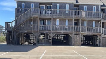 A multi-story building with balconies, a parking area, and a beach view.