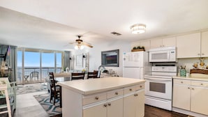 A kitchen with a central island, white cabinets, a microwave, and an oven. There is a dining area with chairs and a table. - 0602 Waters Edge Resort Studio Bedroom Condo by RedAwning (Murrells Inlet)