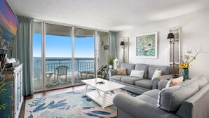 A living room with a sofa, a coffee table, and a view of the sea through a sliding glass door. - 0602 Waters Edge Resort Studio Bedroom Condo by RedAwning (Murrells Inlet)