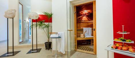 A modern bathroom with a glass shower, a wooden vanity, a towel rack, a potted plant, and a fruit display.