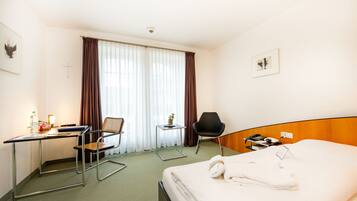 Habitación de hotel con cama, escritorio, dos sillas, una mesita y ventana con cortinas.