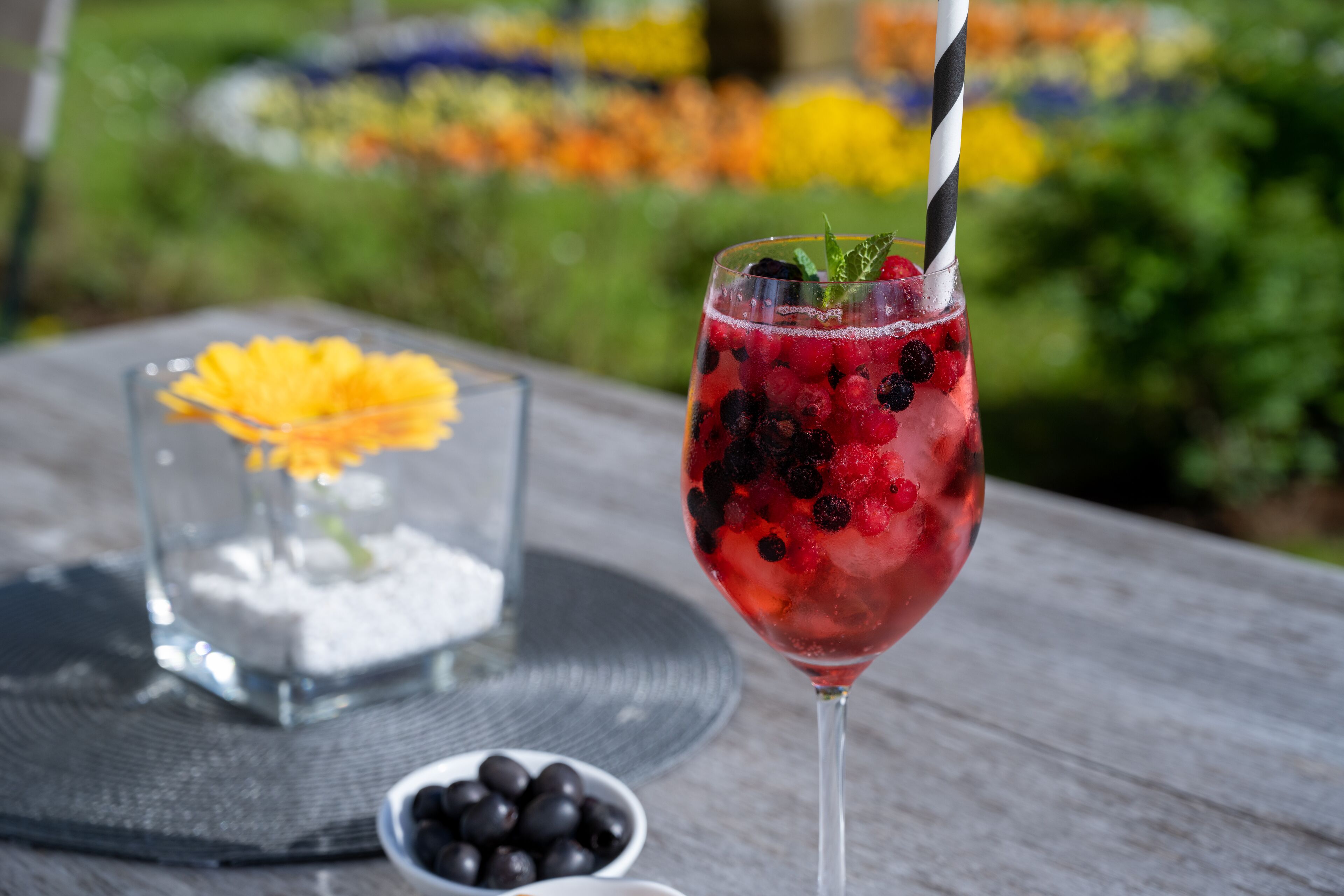 A glass of red beverage with berries and a mint garnish on a wooden table.