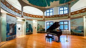 Een statige zaal met een vleugelpiano, hoge plafonds en versierde muurschilderingen.