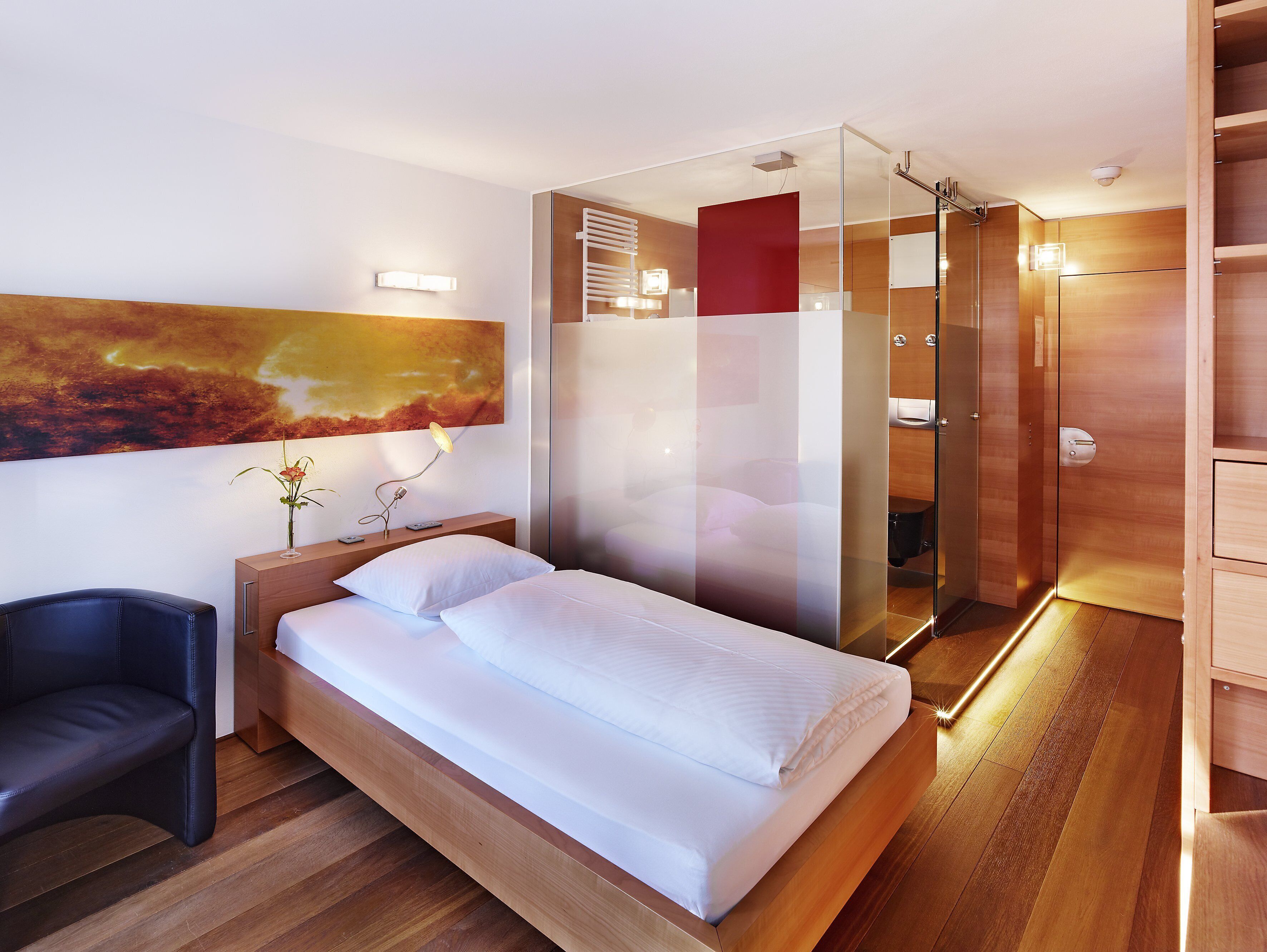 A modern hotel room with a wooden bed, a glass shower enclosure, and a large abstract painting on the wall.