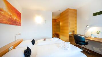 A hotel room with two beds, a desk, a chair, and a large painting on the wall.