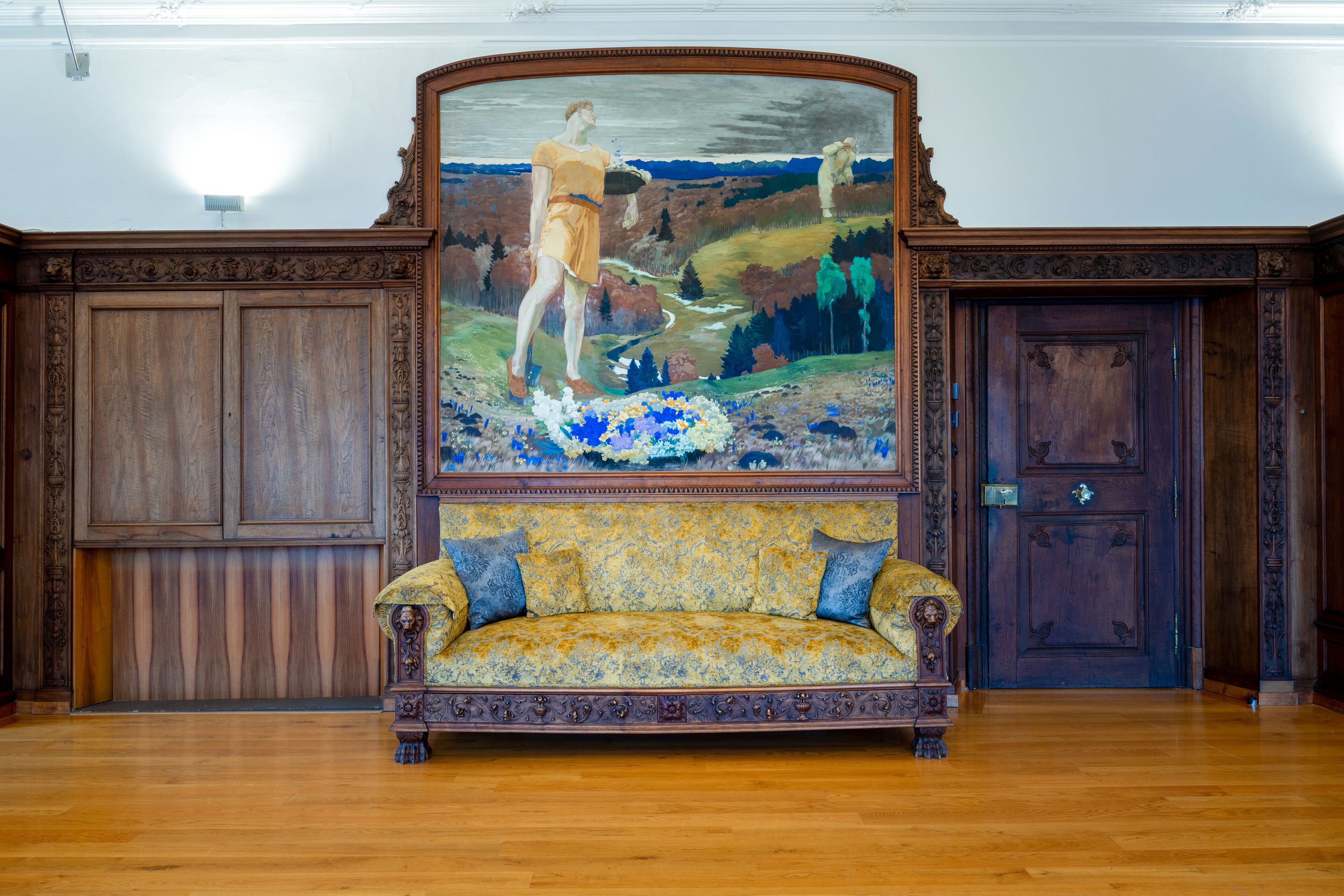 A room with a large painting, a wooden floor, and a sofa with patterned upholstery.