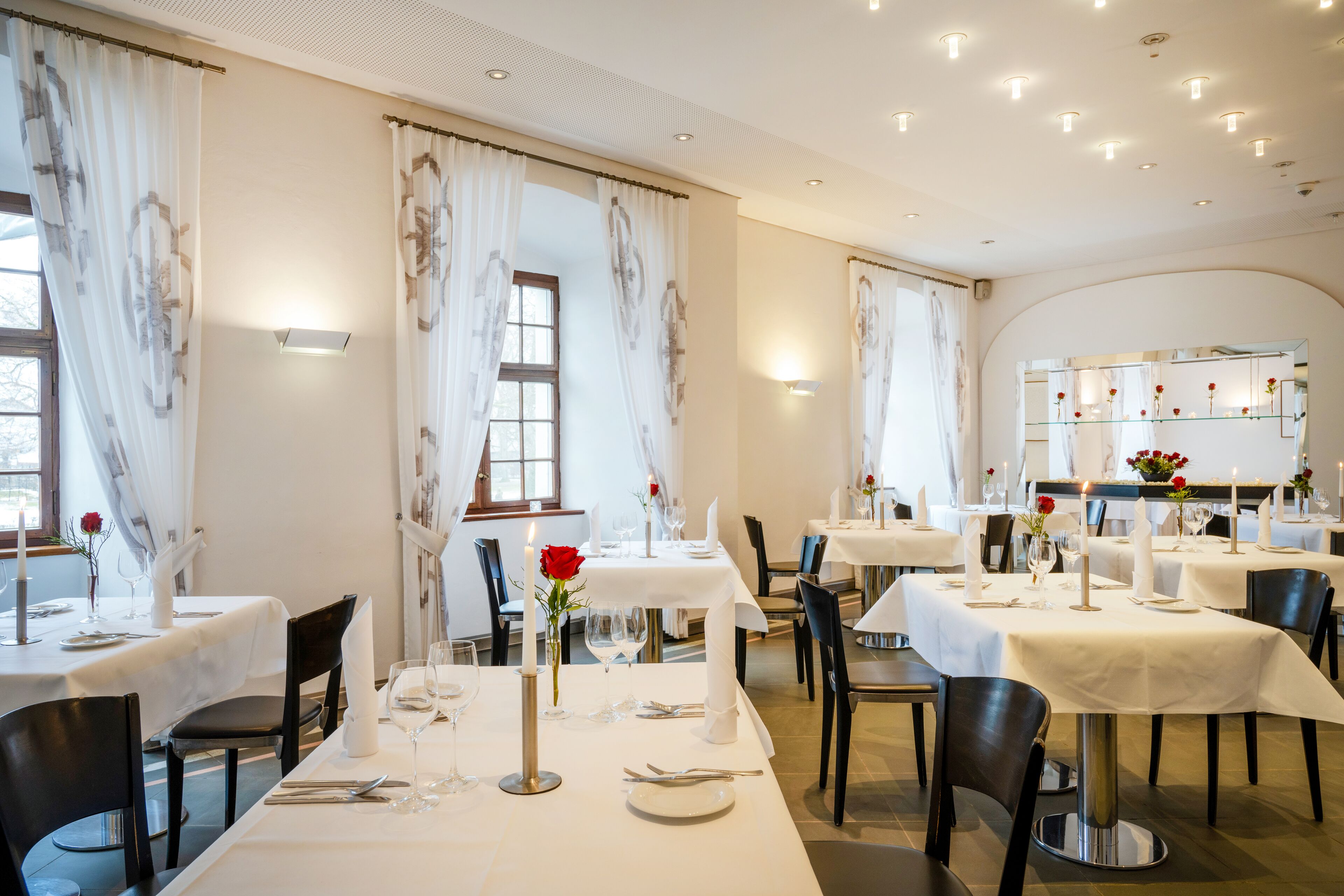 Un restaurante con varias mesas dispuestas para comer, con manteles blancos y centros de mesa con velas.