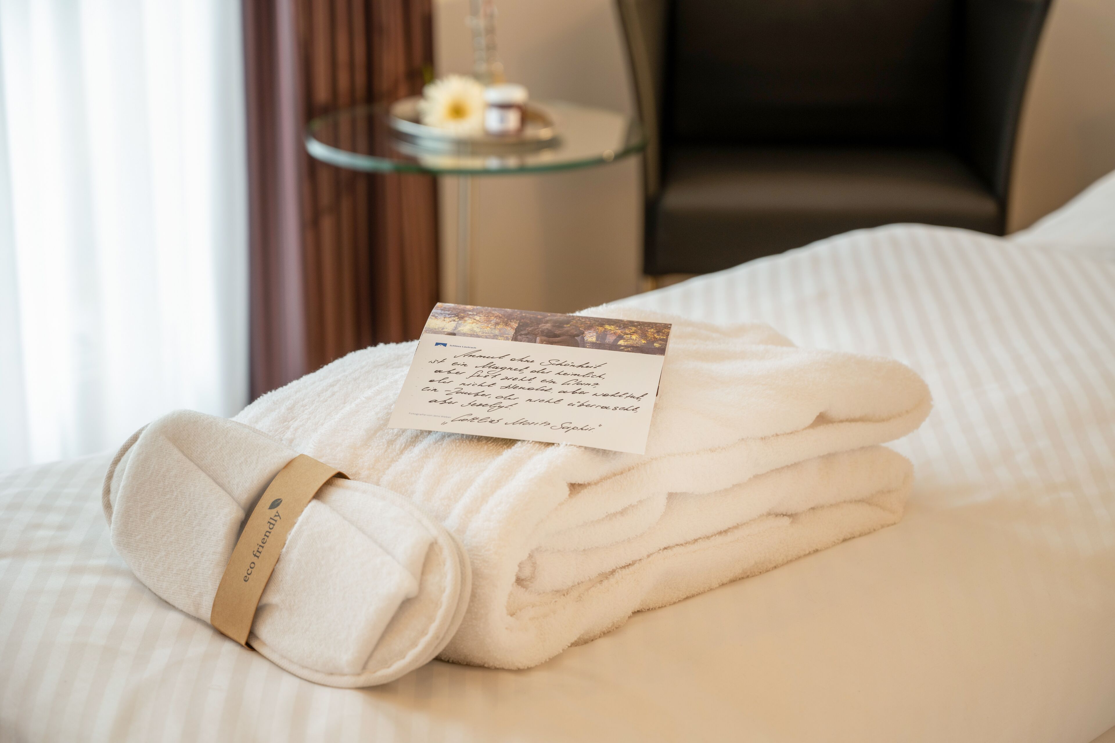 A neatly folded set of white towels with a tag labeled "eco friendly" on a bed.