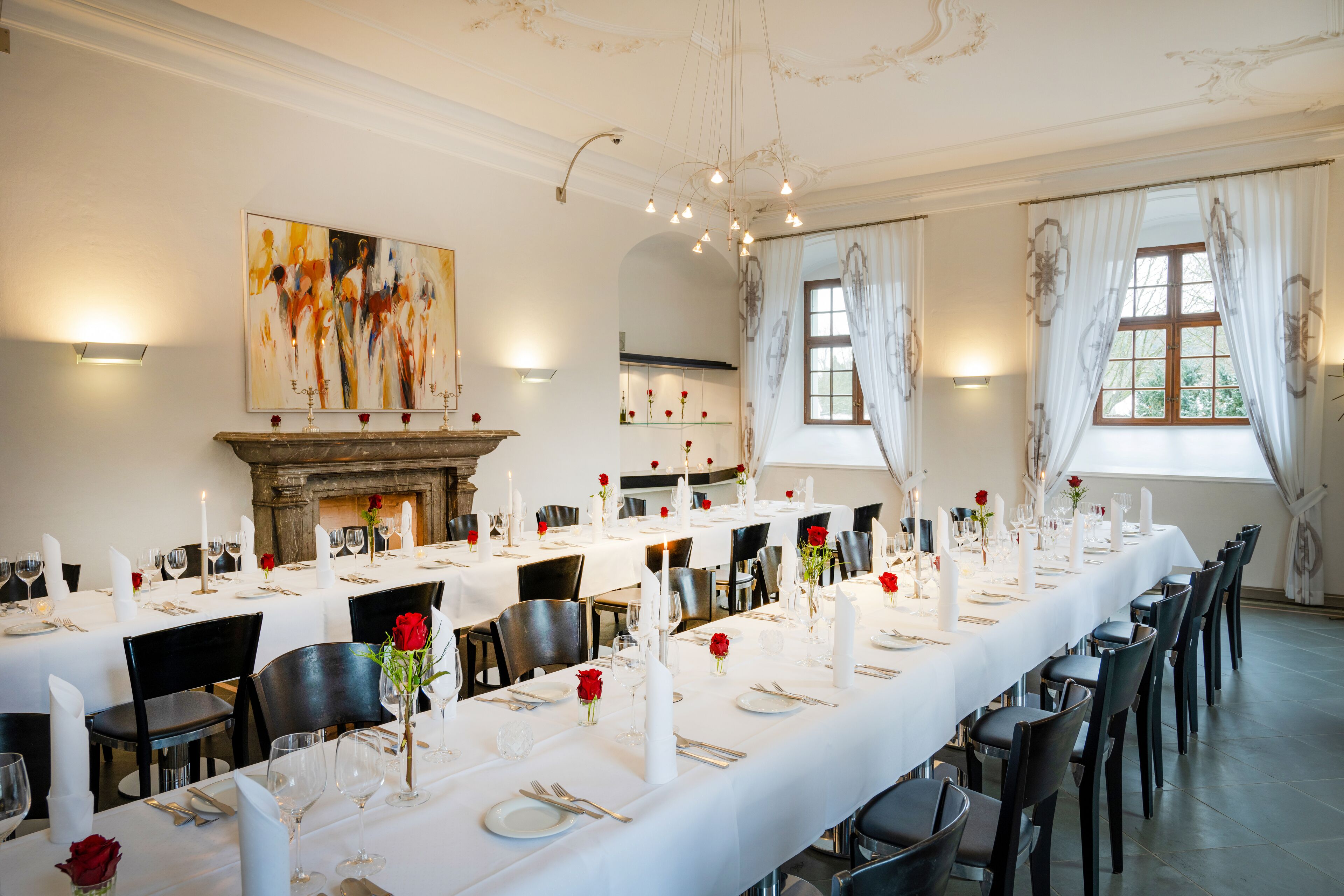 A formal dining room with long tables set for a meal, a fireplace, and a large abstract painting on the wall.