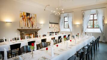 A formal dining room with long tables set for a meal, a fireplace, and a large abstract painting on the wall.