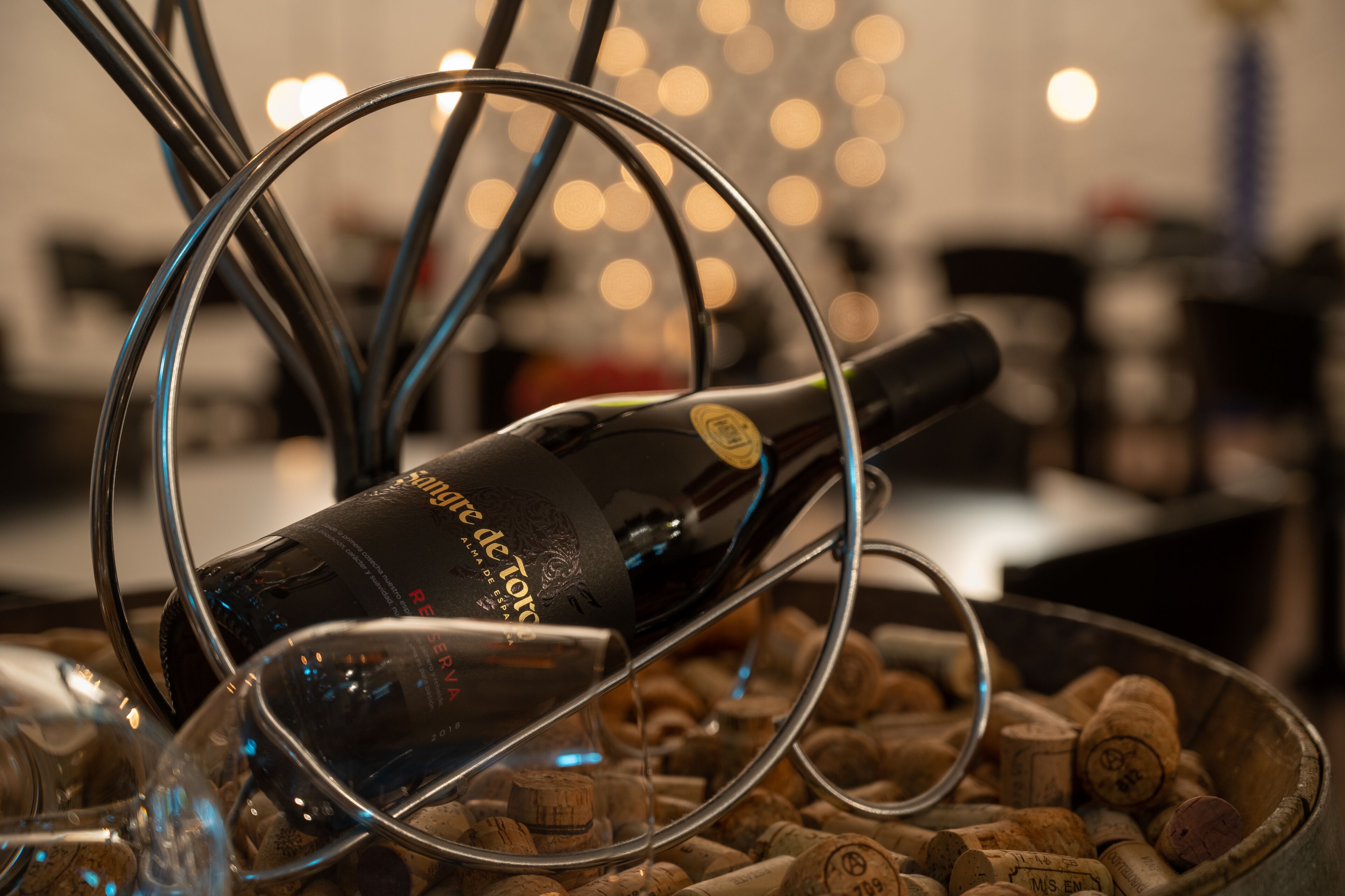 A bottle of wine with a corkscrew and wine glasses on a table with corks.