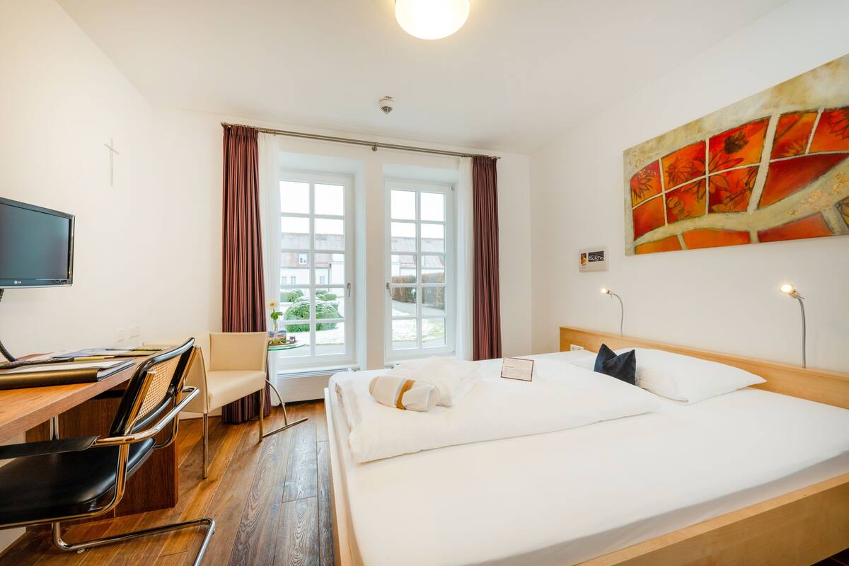 Een hotelkamer met een bed, bureau, stoel en een groot raam met gordijnen.