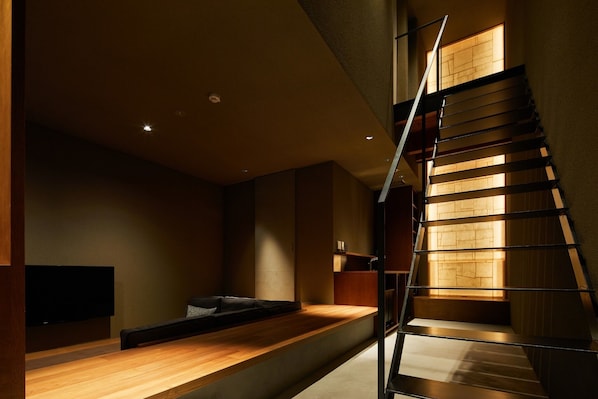 A modern interior with a wooden staircase, a flat-screen TV, and a minimalist seating area.