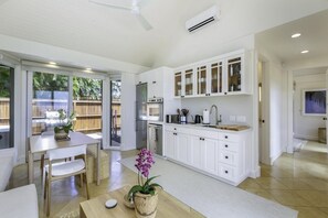 Une cuisine moderne avec des meubles blancs, un coin repas comprenant une table et des chaises, et un ventilateur de plafond.