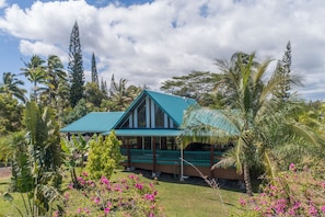 Une maison dotée d’un toit végétalisé et d’un porche, entourée d’une végétation tropicale.