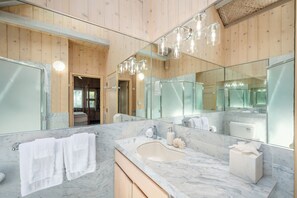 Un baño moderno con paredes de madera, un espejo grande, un lavabo de mármol y zona de ducha.
