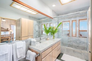 Un baño moderno con ducha de vidrio, encimeras de mármol y un espejo grande.