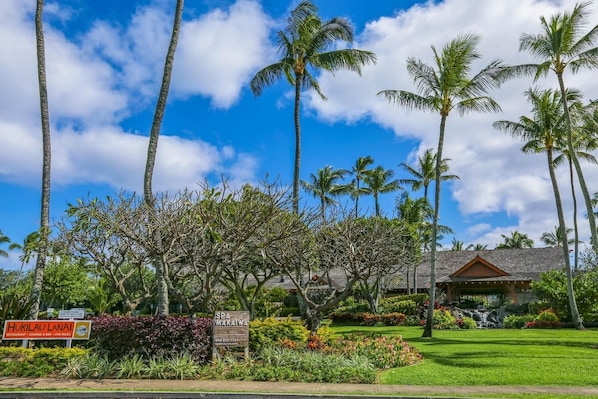 Un resort tropical con palmeras, un letrero que indica el spa 'Hukilao Lanai' y un edificio con techo de paja.