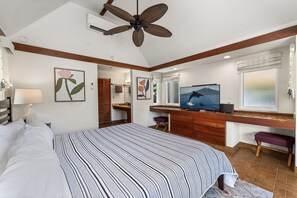 Ein Schlafzimmer mit einem großen Bett, einem Schreibtisch mit Computer, einem Fernseher und einem Deckenventilator.