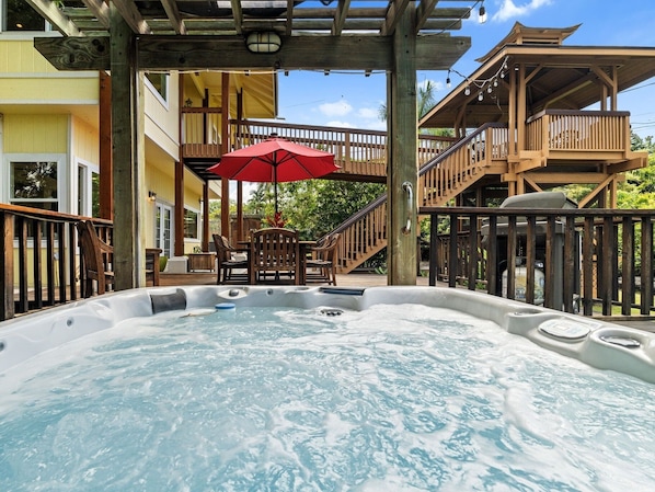 Ein Whirlpoolbereich mit Holzterrasse, Sitzgelegenheit im Freien und einem roten Sonnenschirm.
