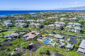 An aerial view of a resort with multiple buildings, a swimming pool, and a view of the ocean.