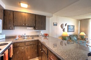 A kitchen with granite countertops, wooden cabinets, and a built-in stove. There is a dining area with a sofa and two lamps.