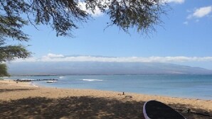 A beach with a surfboard on the sand and a clear view of the ocean and distant mountains. - Maalaea Kai 316 1 Bedroom Condo by RedAwning (Wailuku)