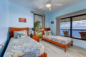 Un dormitorio con dos camas, ventilador de techo, ventana con persianas y vista al océano.