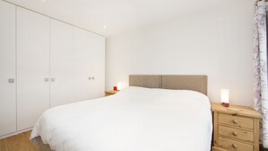 A bedroom with a large bed, wooden nightstands, a wardrobe, and a night lamp. - Up-market one Bedroom Apartment Just Minutes From the River Thames. Broughton rd (London)