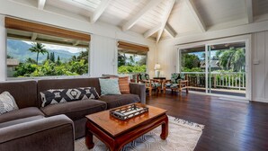 A spacious living room with a large sofa, coffee table, and a view of lush greenery and mountains through large windows. - Hale Naninoa 5 Bedroom Home by RedAwning (Hanalei)