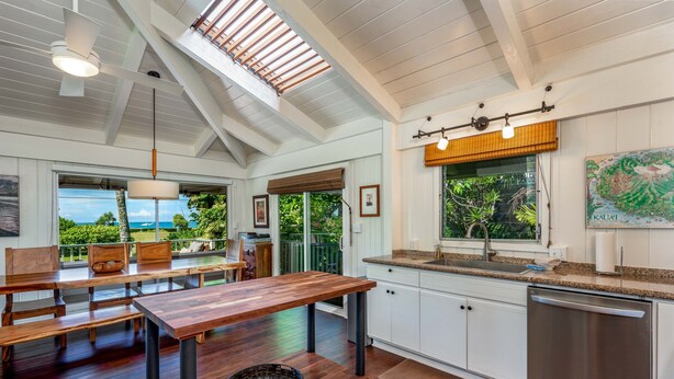 A modern kitchen with white cabinets, a wooden dining table, and a view of the outdoors. - Hale Naninoa 5 Bedroom Home by RedAwning (Hanalei)