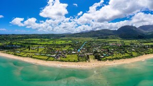 An aerial view of a coastal resort with a beach, golf course, and mountainous backdrop. - Hale Naninoa 5 Bedroom Home by RedAwning (Hanalei)