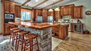 Una cocina con armarios de madera, una isla de piedra con taburetes y un ventanal amplio.