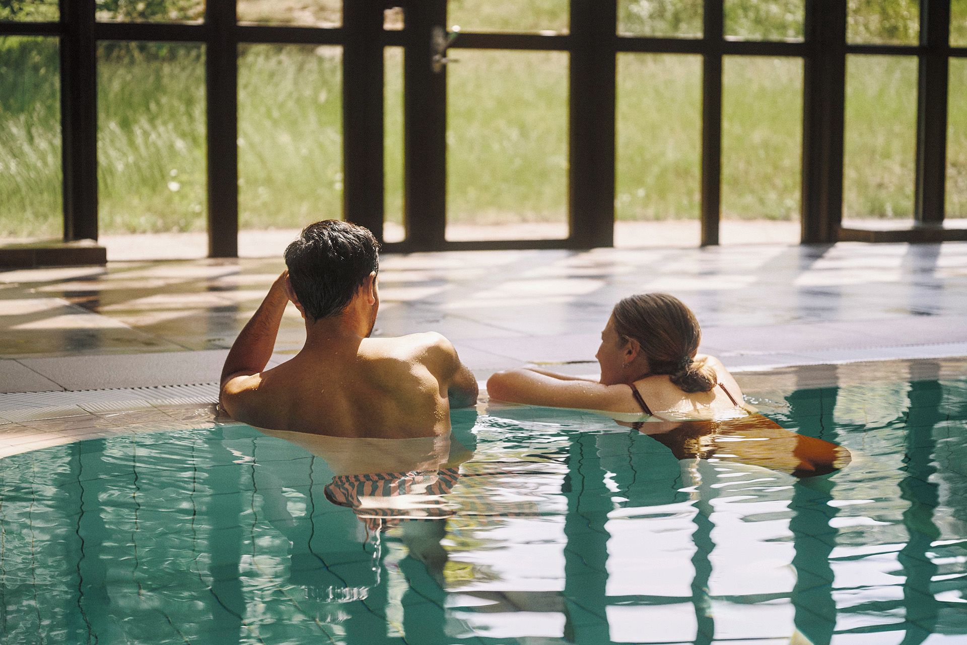 A swimming pool with clear water, surrounded by a tiled floor and large windows.