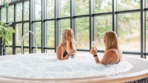 Two people in a hot tub with a view of greenery through large windows. - Rönneberga (Lidingo)