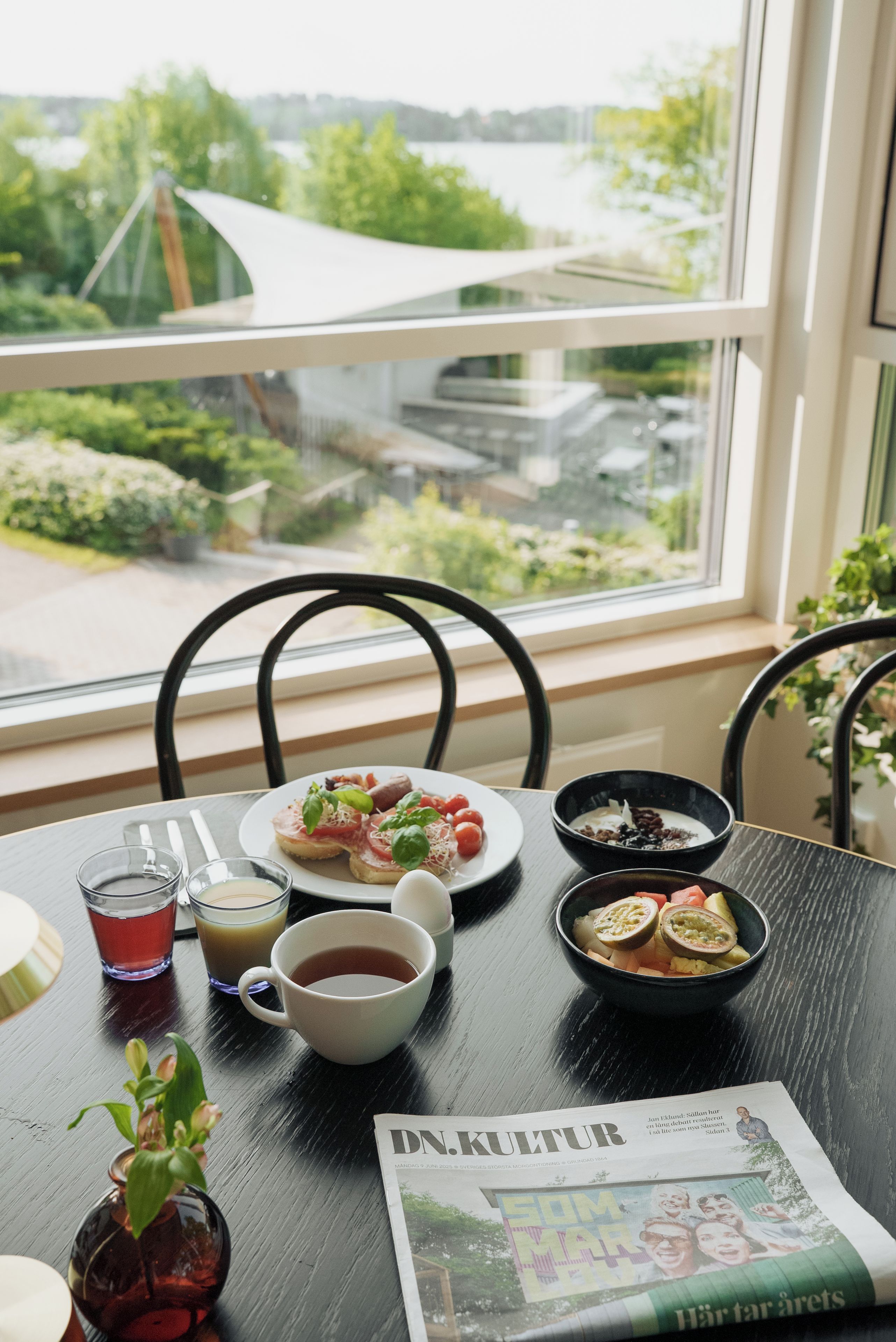 A dining table with plates of food, glasses, and a newspaper.