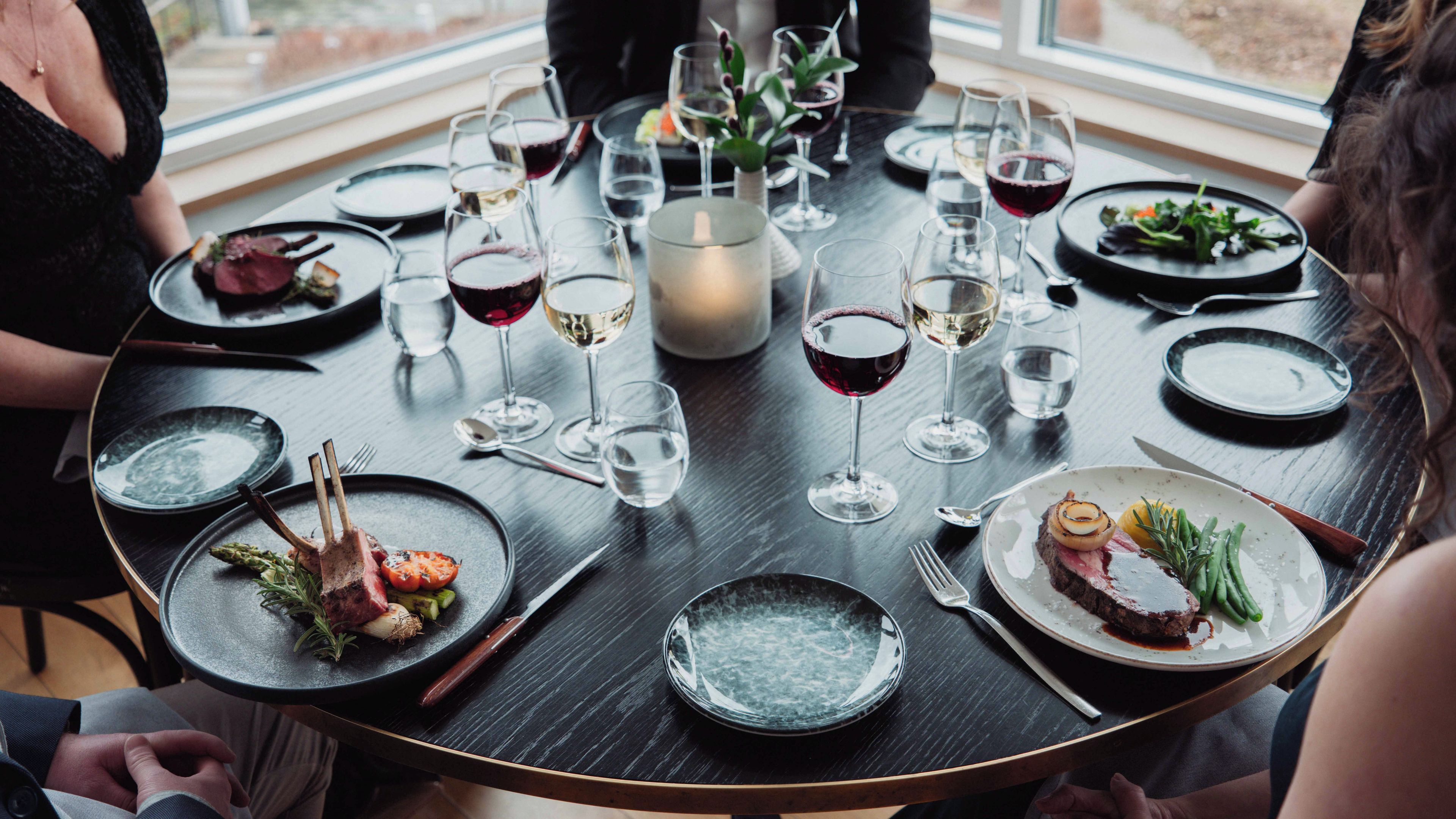 A round dining table with plates of food, wine glasses, and cutlery.