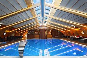 An indoor swimming pool with a high, sloped ceiling and wooden beams. - Rönneberga (Lidingo)