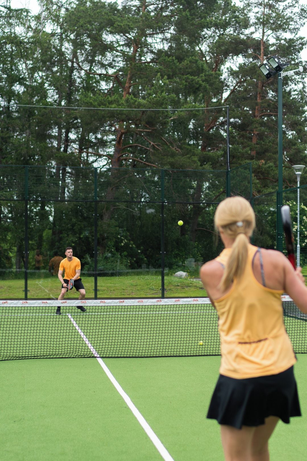 A tennis court with a net, surrounded by a fence and trees.