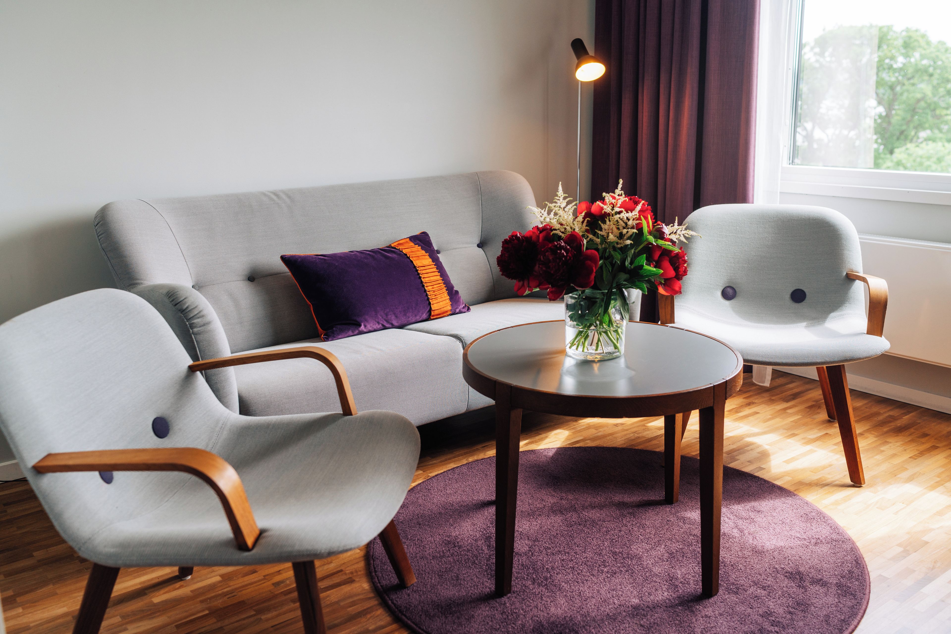 Una sala de estar moderna con un sofá gris, dos sillones, una mesa de centro redonda y un jarrón con flores.