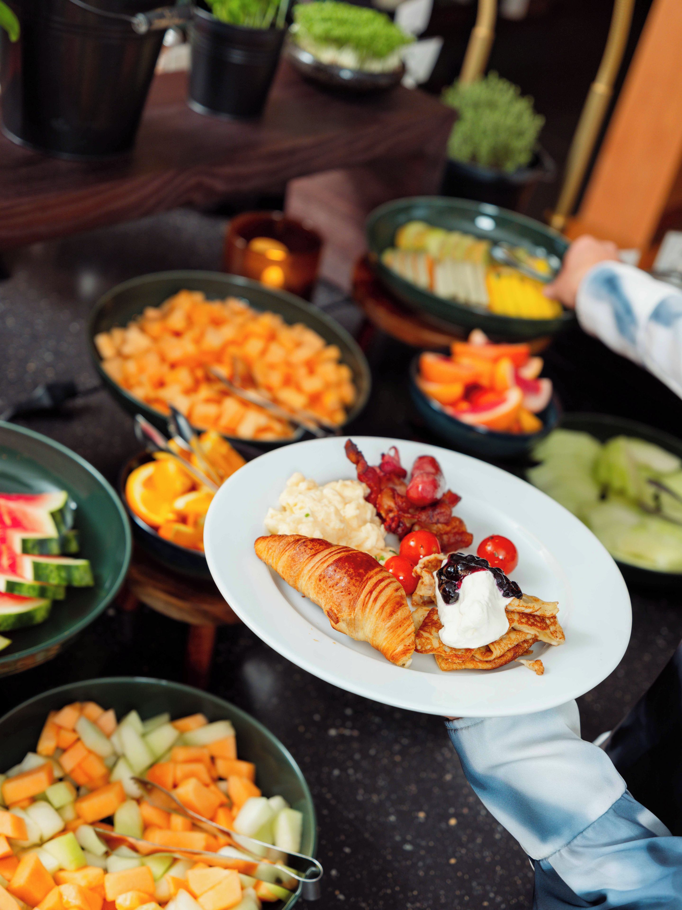 Una mesa de buffet con diversas opciones de comida, incluyendo frutas, verduras y un plato con un croissant y bayas.