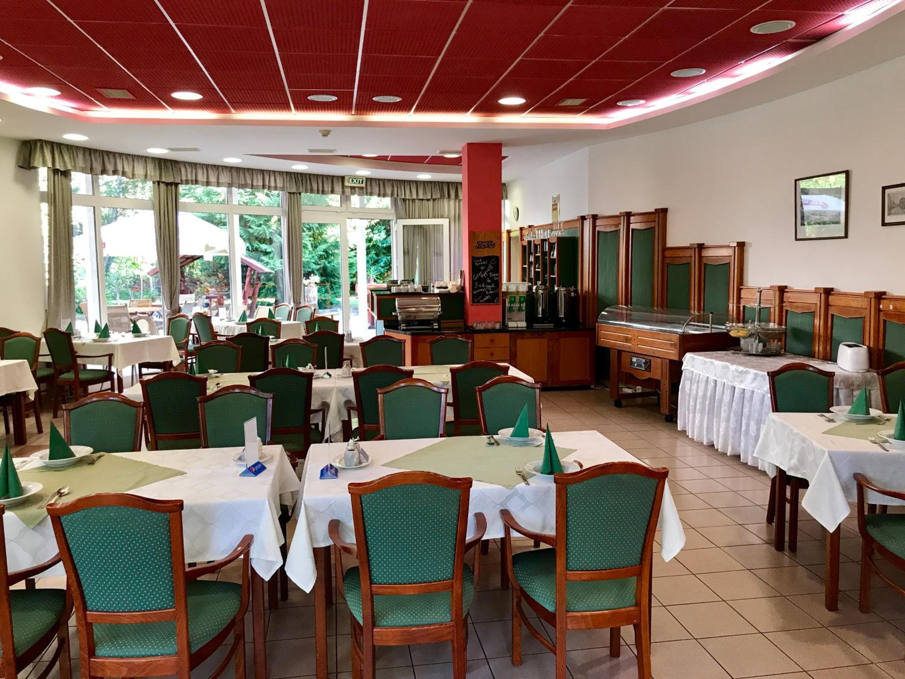 Uma área de refeições com várias mesas e cadeiras, um buffet e vista para o exterior.