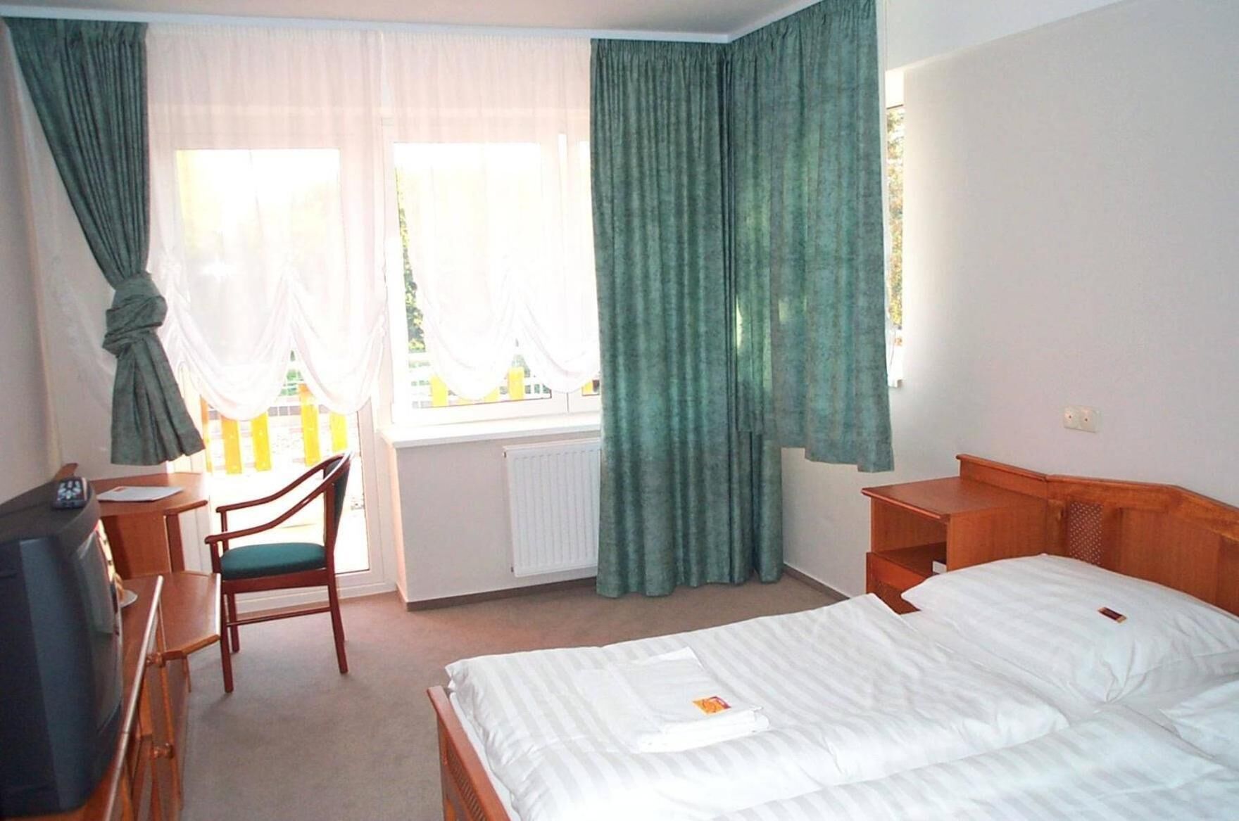 A hotel room with a bed, a desk, a chair, and a window with curtains.