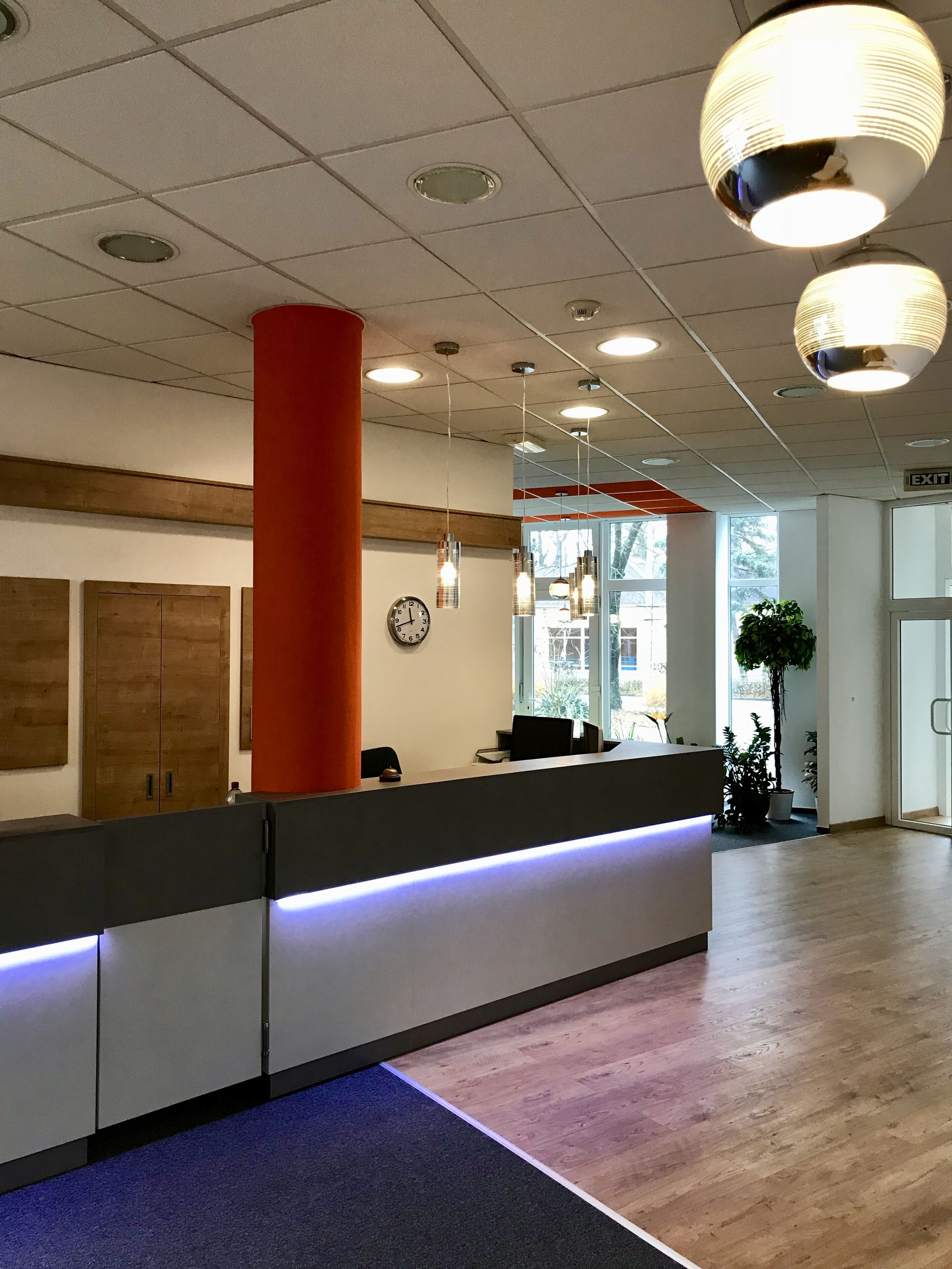 Un espace d’accueil avec un comptoir, une horloge et un grand pilier rouge.