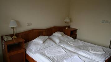 A double bed with white linens, two bedside lamps, a wooden nightstand with a telephone, and a small shelf.
