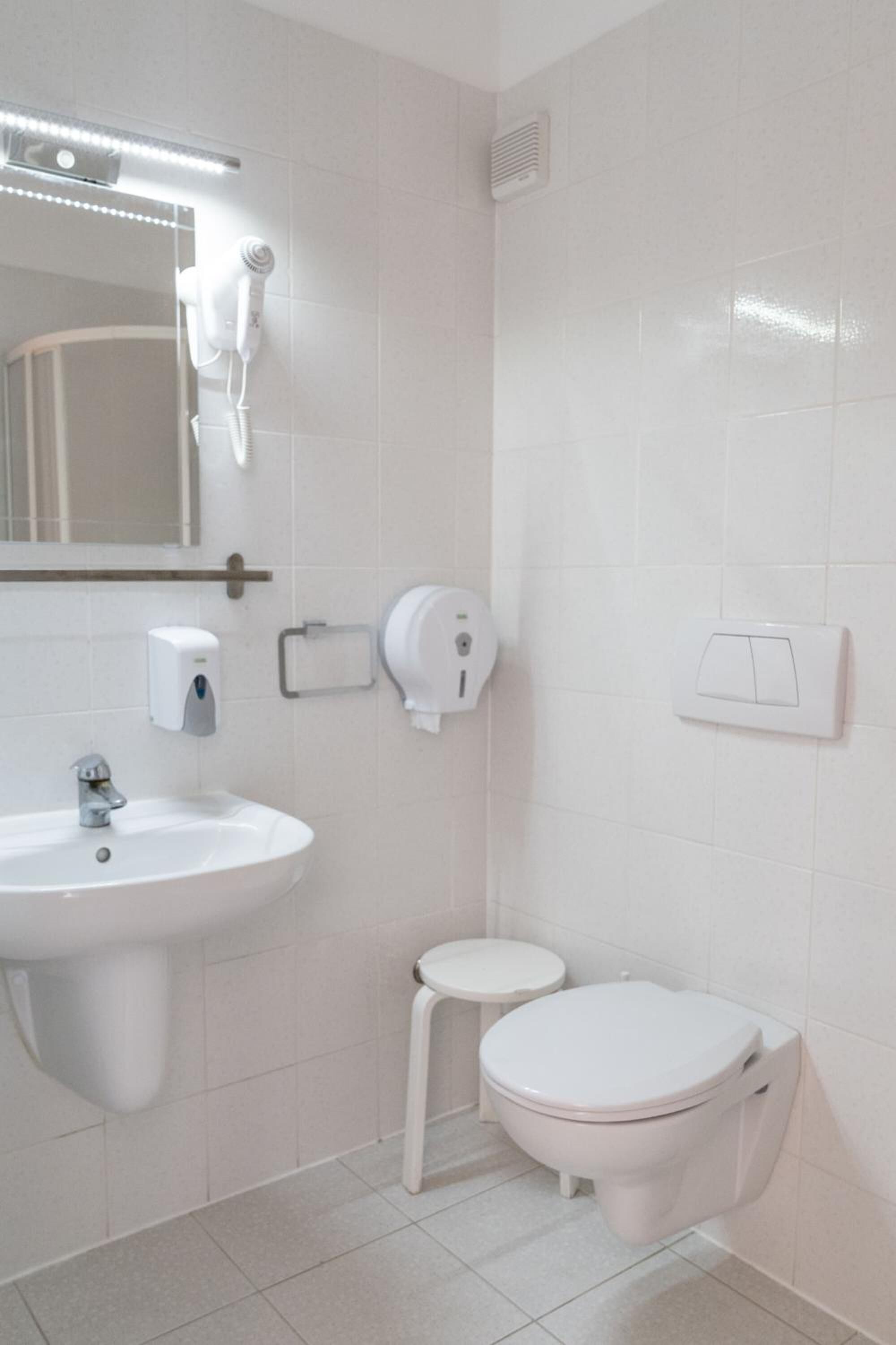 A bathroom with a white sink, a toilet, a hand dryer, and a mirror.